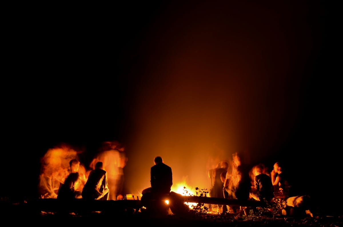Menschen sitzen abends um ein Lagerfeuer