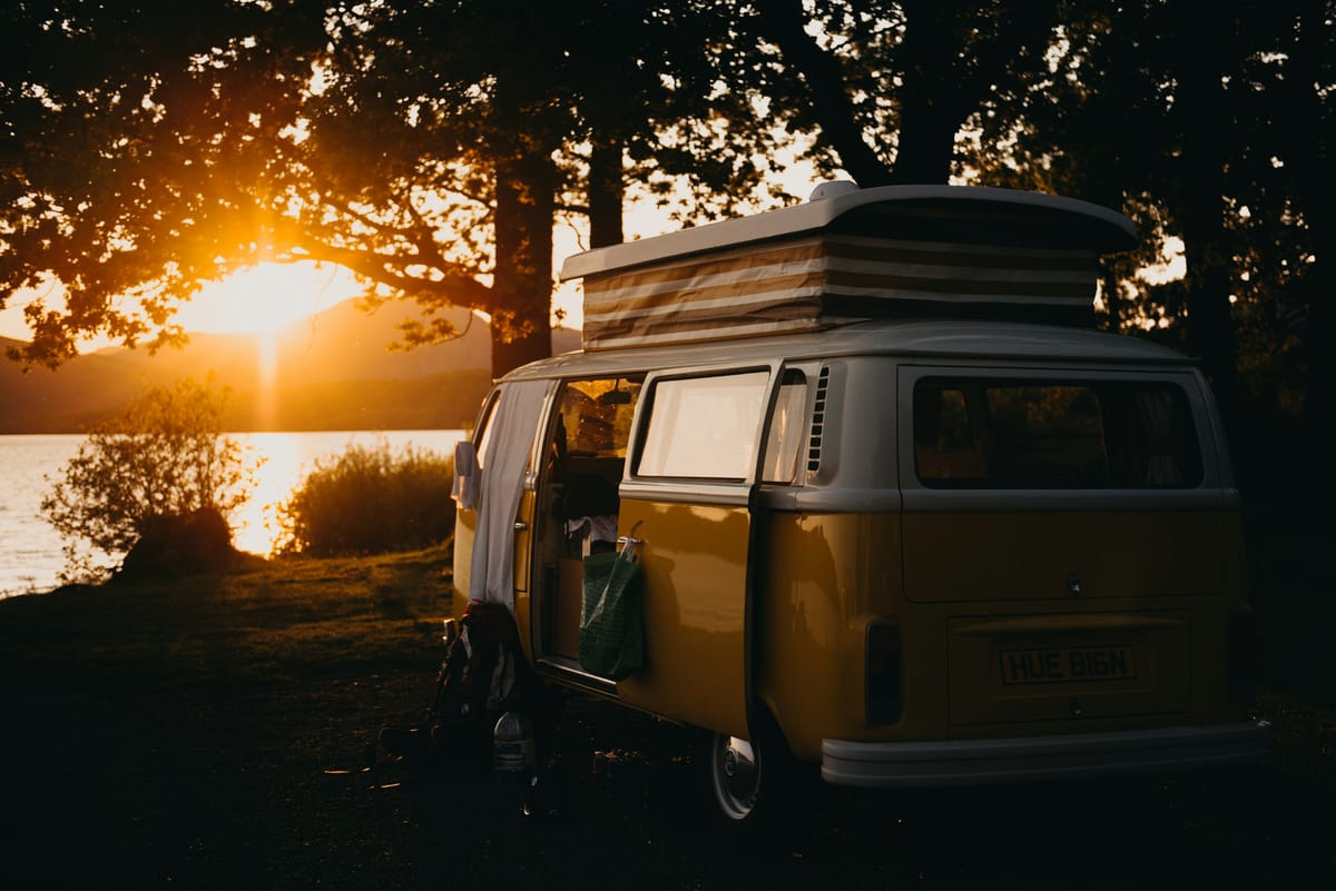 Campingbus unter Baeumen im Gegenlicht der Abendsonne